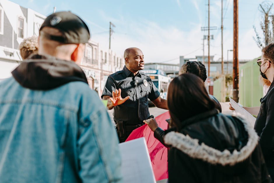 A police officer engaging in conversation with protesters on a sunny street.
