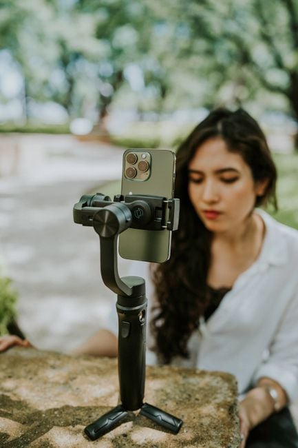 Woman interacts with smartphone on gimbal outdoors in sunlit setting.
