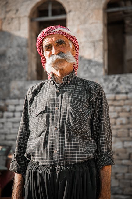 Portrait of an elderly man with a mustache in Syria wearing traditional attire, posing outside on a sunny day.