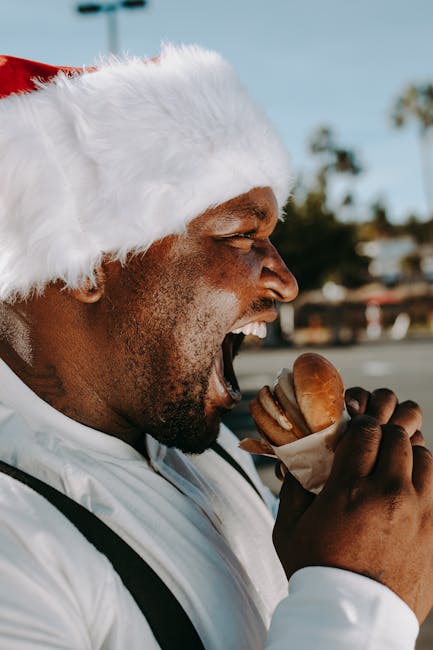 A joyful man in a Santa hat relishes a burger outside during the festive season.