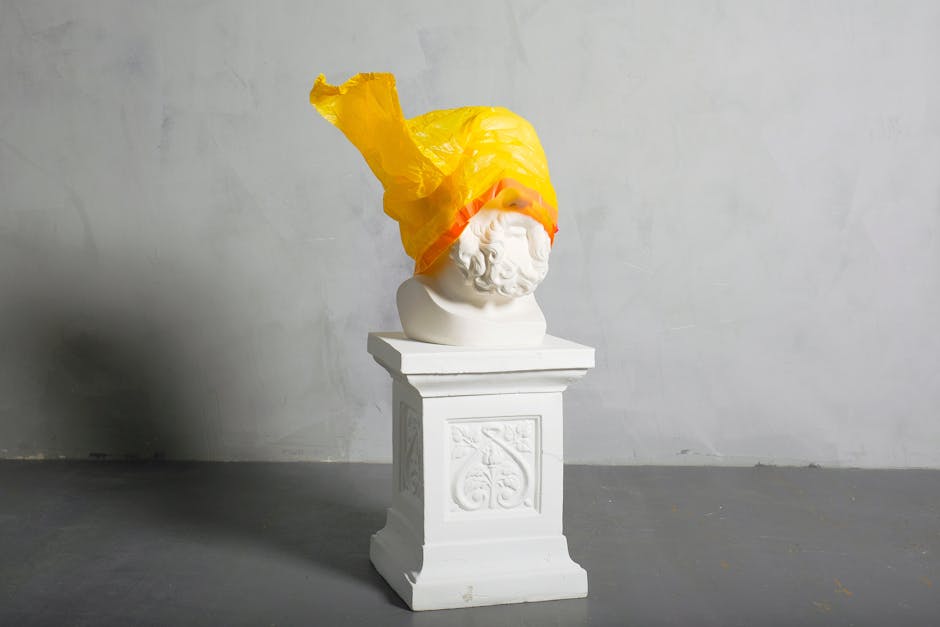 A classical marble bust adorned with a vibrant yellow plastic bag, creating a striking visual statement.
