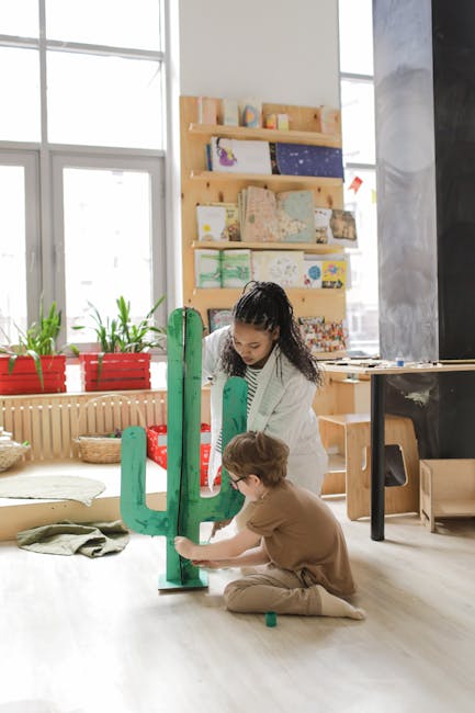 A teacher assists a child in crafting a large green cactus model in a classroom setting.