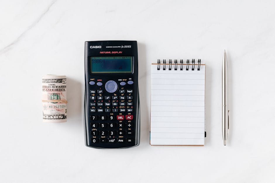 Top view of financial tools including a calculator, notepad, pen, and rolled cash on a white background.