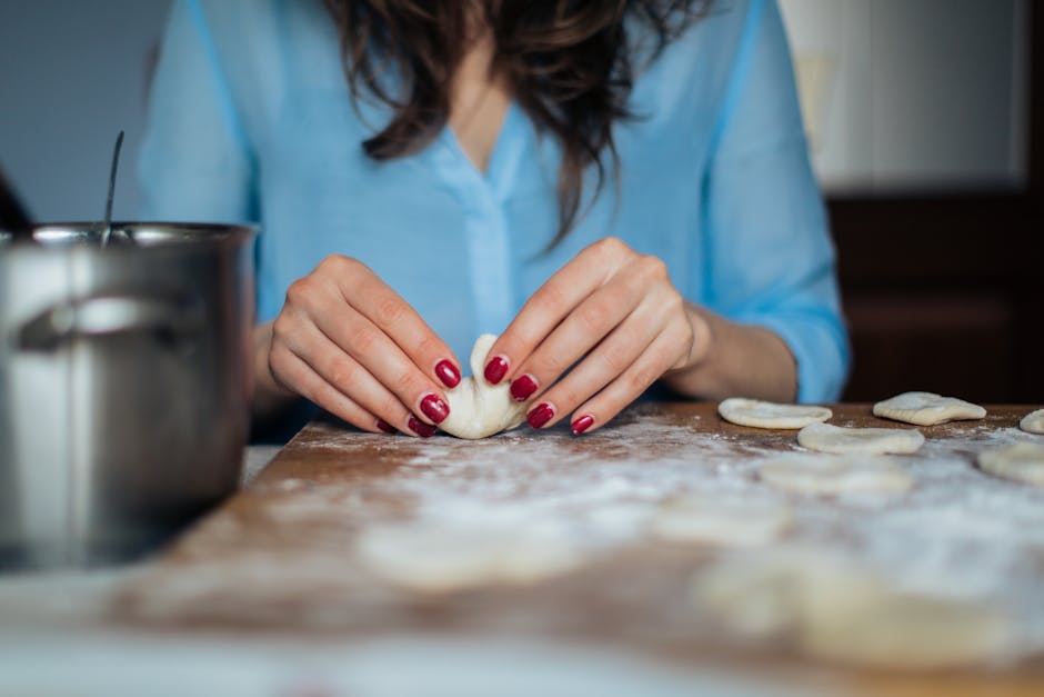 A woman skillfully shaping homemade dumplings on a wooden surface covered with flour.