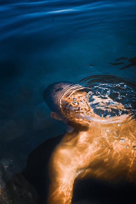 A man swimming peacefully underwater as sunlight creates beautiful patterns on the water surface.