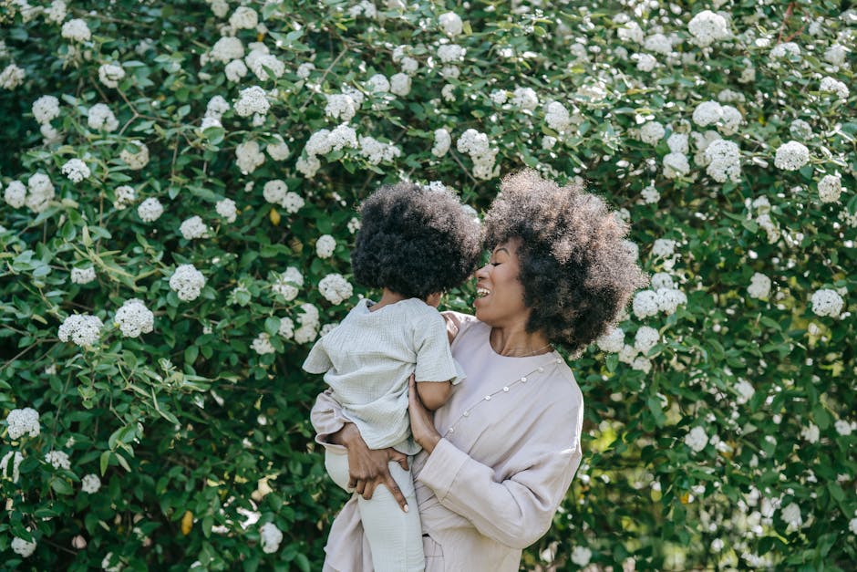 A joyful moment between mother and child with afro hair, surrounded by blossoming flowers.