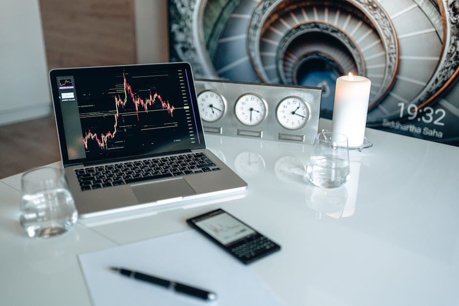 A modern desk setup featuring a laptop displaying trading charts, candles, and clocks.