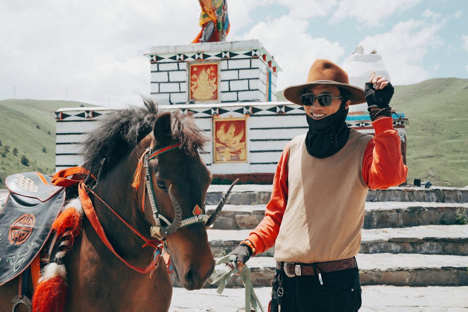 A Tibetan man with his horse poses in traditional attire in the scenic outdoors of Sichuan, China.