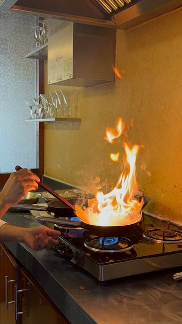 A chef flambéing a dish on a stove in a modern kitchen with bright flames.
