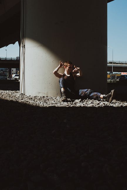 A dancer poses expressively under a city bridge with industrial vibes.