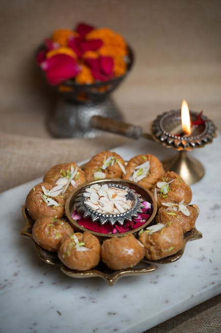 Indian sweets on a tray with flowers and a lit diya; perfect for cultural festivities.