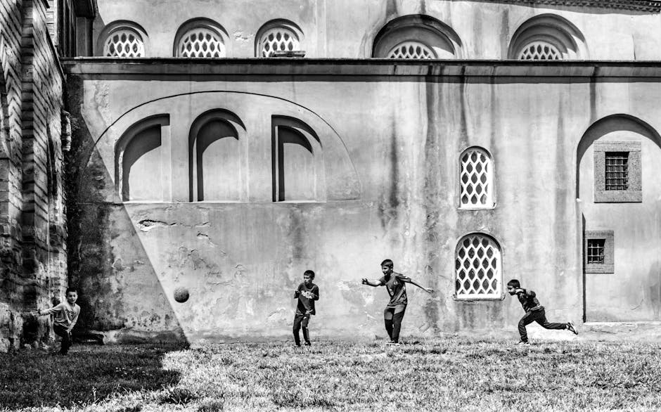 Black and white photo of kids playing football outside a historical mosque in Istanbul.