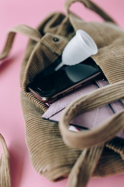 A silicone menstrual cup and smartphone in a corduroy bag on a pink background, emphasizing zero waste lifestyle.