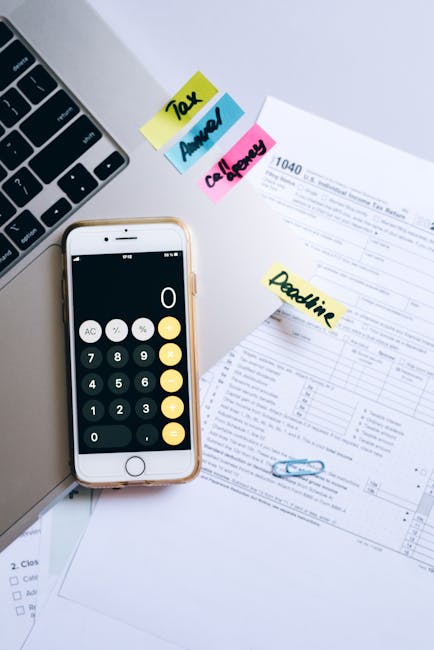 A smartphone calculator and tax forms on a desk, symbolizing financial planning.