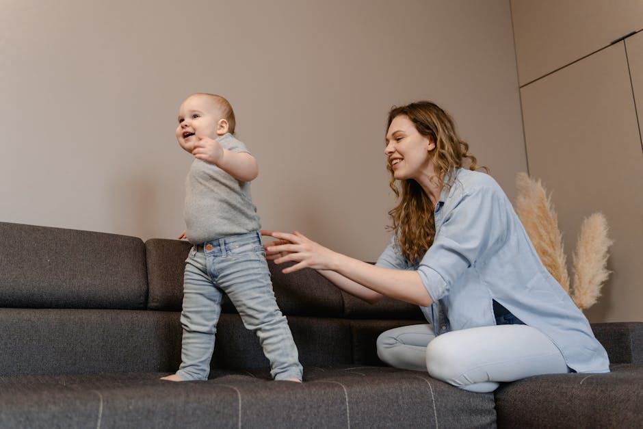 Mom assisting baby in taking first steps on a comfortable sofa indoors.