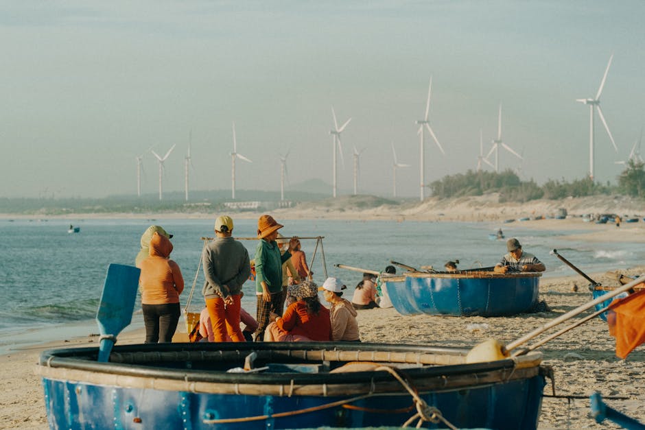 People on a sandy beach with round boats and wind turbines in the background.