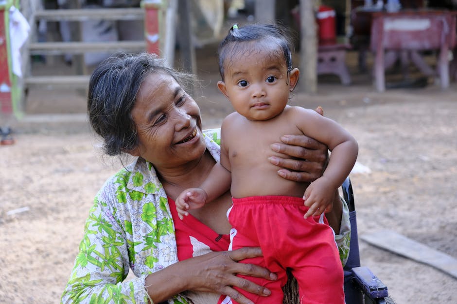 Elderly woman joyfully holding a baby outdoors in Cambodia, capturing a beautiful moment of family bond and happiness.