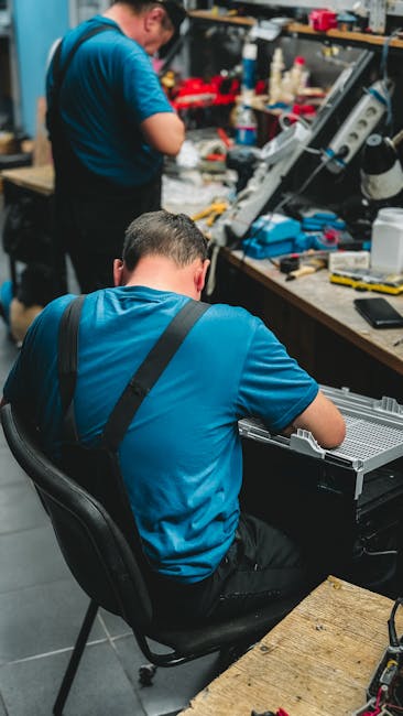 Two technicians repairing electronic devices in a cluttered workshop.