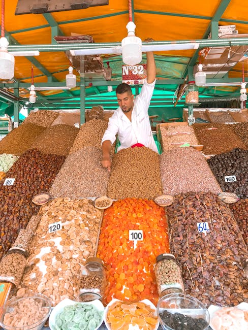 Colorful market stall with diverse dried fruits and nuts arranged in tall piles, attended by a vendor.