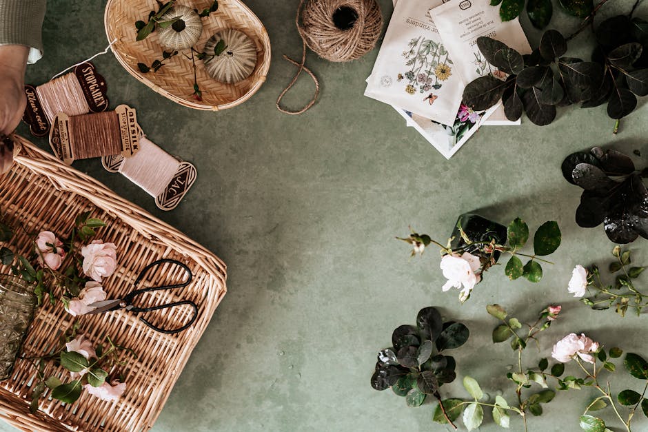 Flat lay of floral arrangement with baskets, roses, and vintage twine on a green surface.