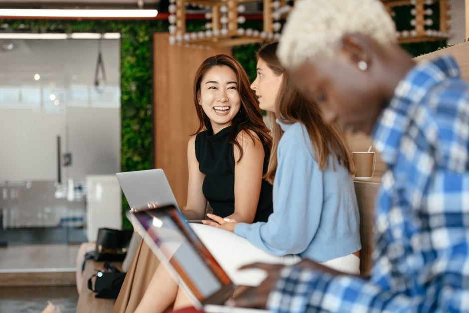 Blurred African American woman browsing laptop while multiethnic cheerful colleagues talking about project in office
