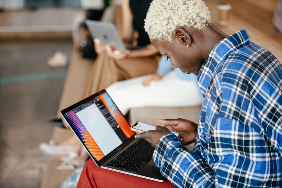 From above of young crop African Amercian female working with netbook while texting message on mobile phone