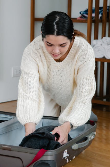 Woman in cozy sweater packing clothes into a suitcase, preparing for travel.