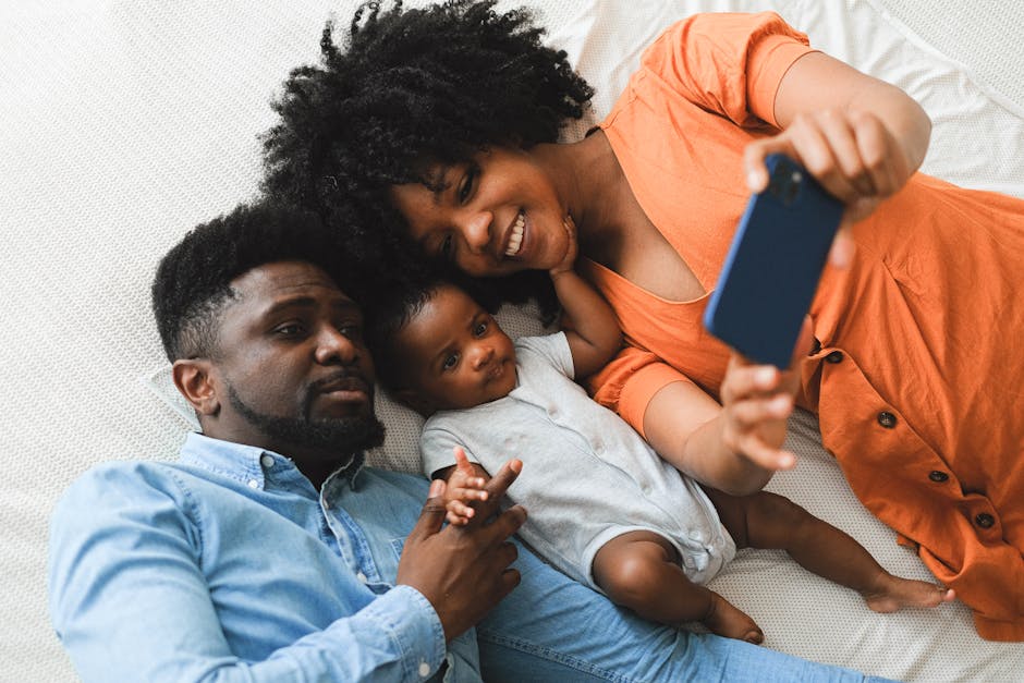 A joyful family moment captured as parents and their baby take a selfie together indoors.