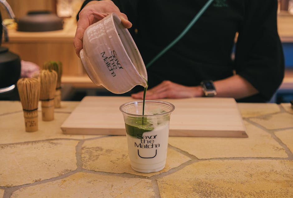 A barista pouring matcha green tea latte into a cup indoors. Enjoy the art of matcha preparation.
