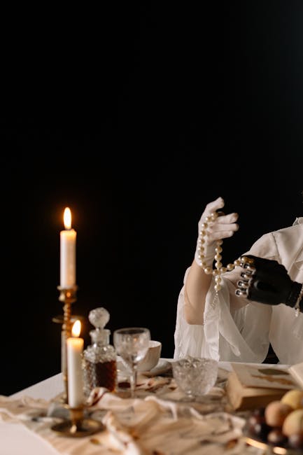 An elegant dark-themed table setting featuring a candlelit ambiance and a hand with a prosthetic arm holding a pearl necklace.
