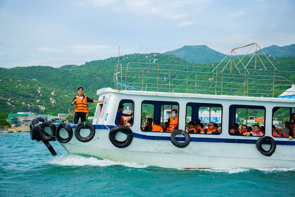 Tourists wearing life vests enjoy a scenic boat ride with lush green hills in the background.