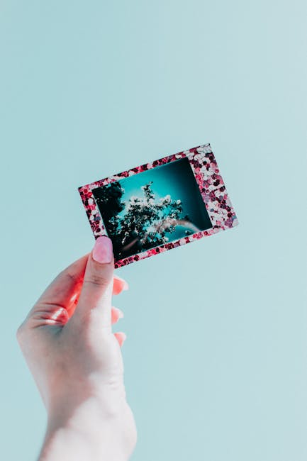 A hand holding a polaroid capturing flowers against a pastel background.
