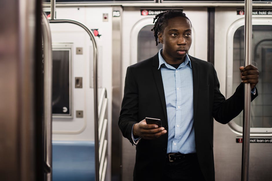 A young man in a suit using his smartphone while commuting on a subway train.