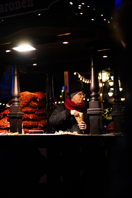 A vendor enjoying a snack at a night market stall full of festive lights and treats.