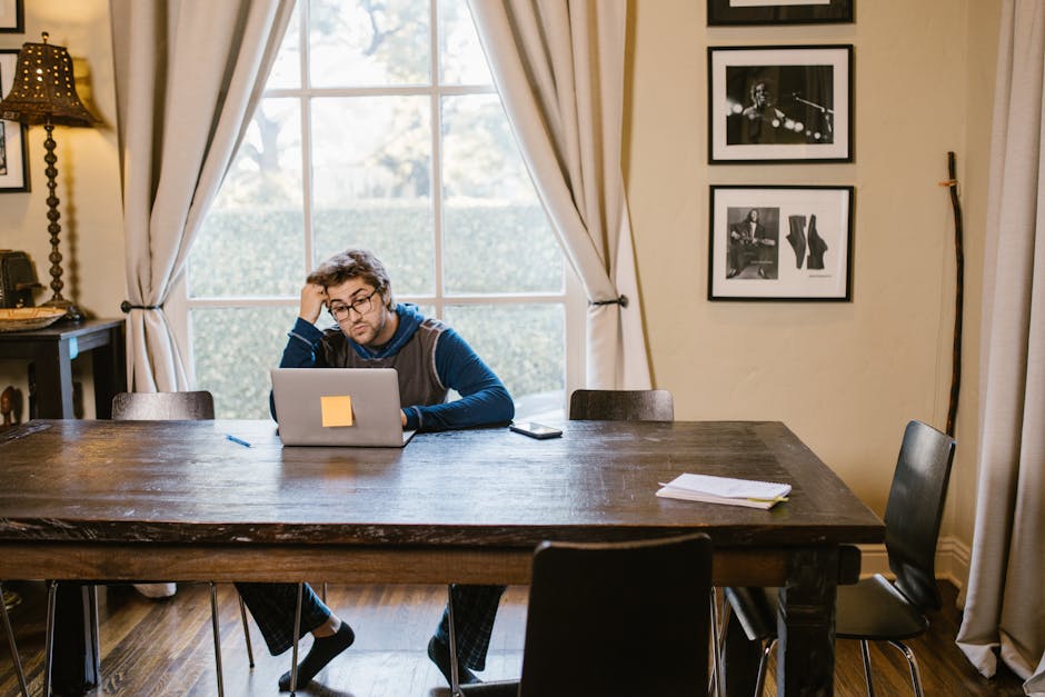Man in casual attire working on a laptop at a wooden table in a cozy room.