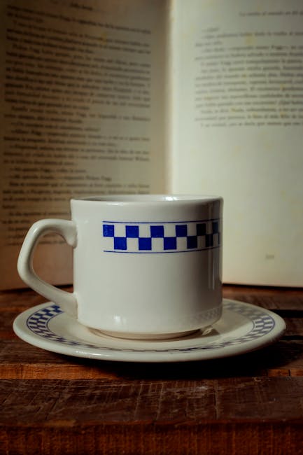 Vintage coffee cup on wooden table with open book in background, creating a cozy reading atmosphere.