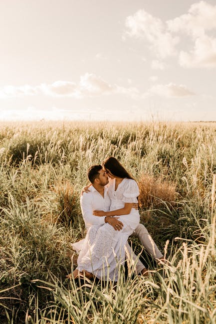 Young couple sharing an intimate moment in a golden grassy field under a bright sky.