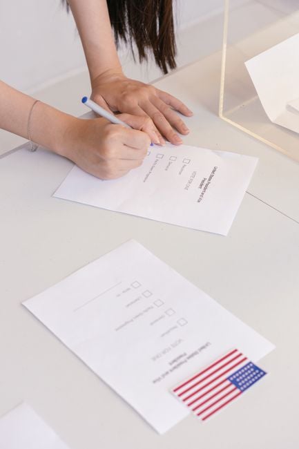 An individual is marking a ballot paper at an election booth, symbolizing democratic participation.