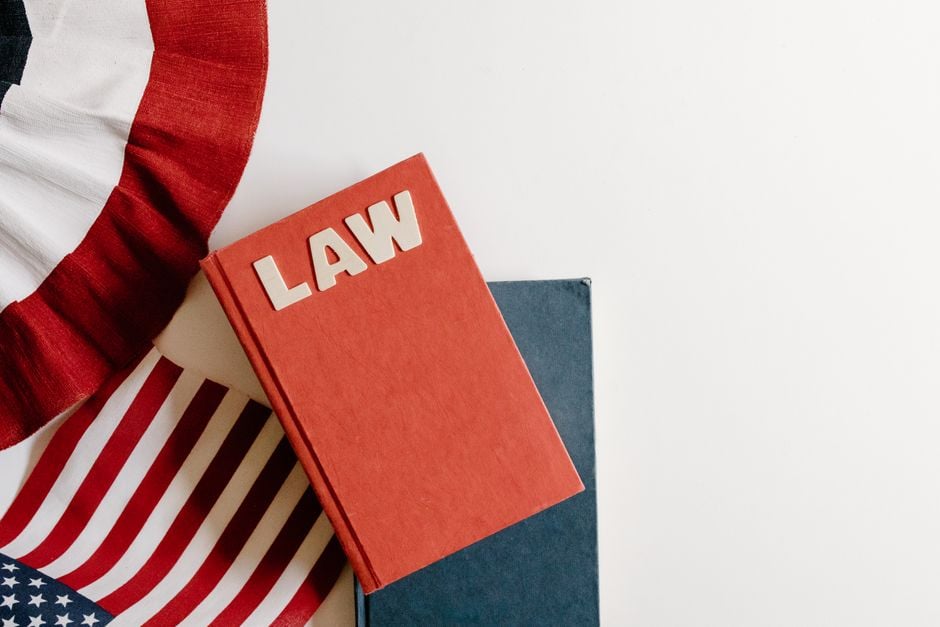 A flat lay of a red law book, American flag, and ribbon displaying patriotic themes.