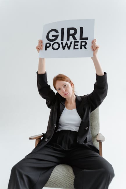 Woman sitting with a 'Girl Power' sign in a black blazer, symbolizing empowerment.