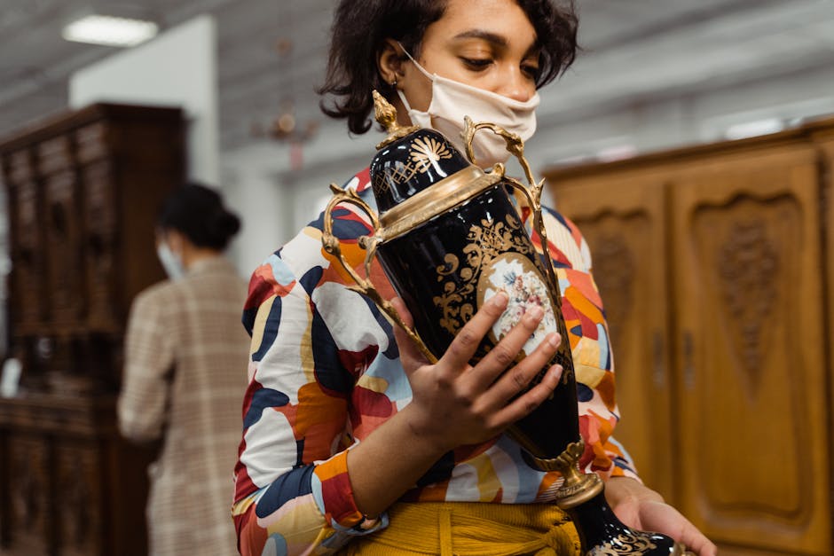 Woman wearing colorful shirt examines ornate vase in a vintage shop.