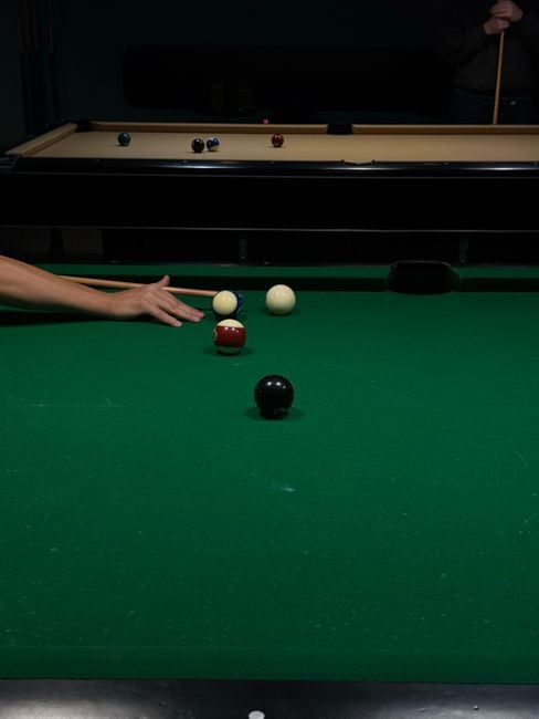 player executing a bank shot during eight-ball practice in a pool hall