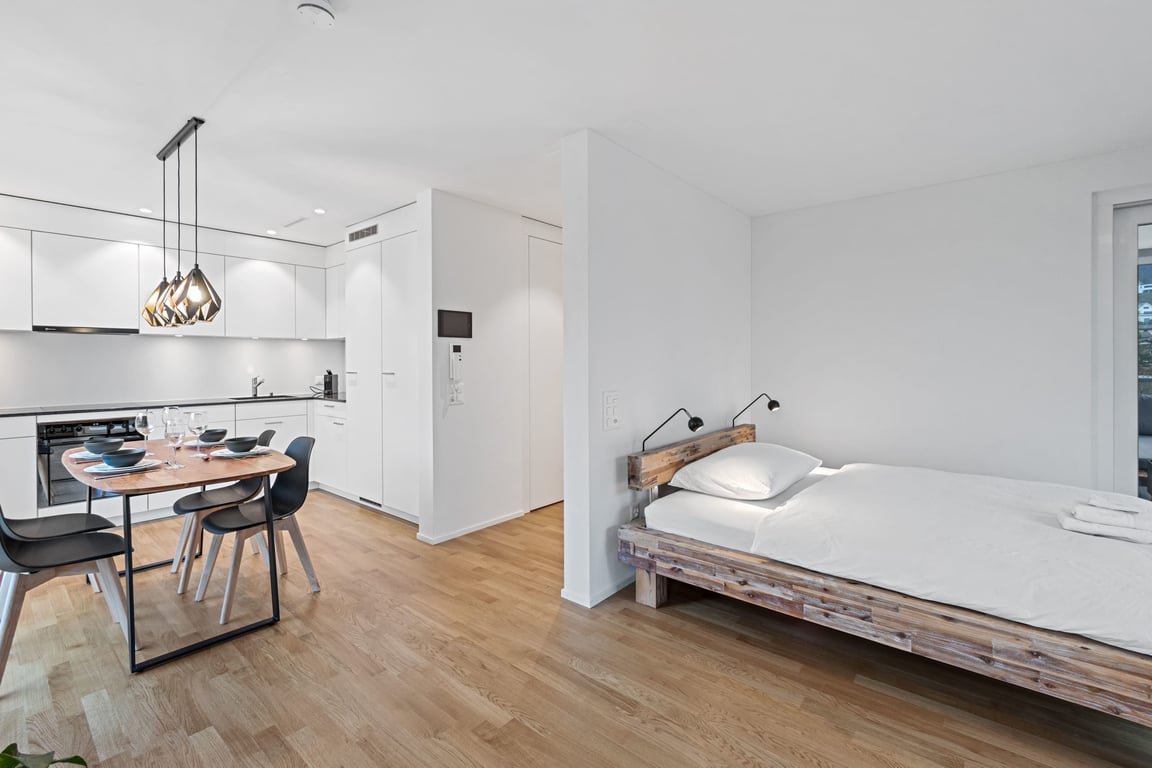 studio apartment with reclaimed wood bed frame white kitchen and round dining table