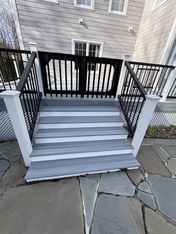 A finished composite deck with black metal railings and stairs down to a flagstone patio