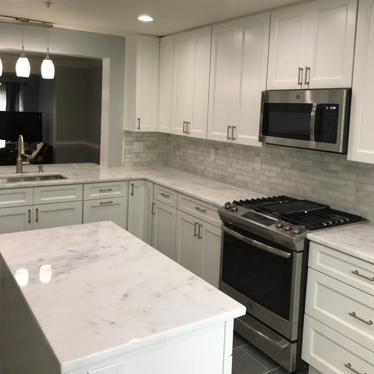 Modern kitchen with white cabinets, marble countertops, stainless steel appliances, pendant lights, and tiled backsplash
