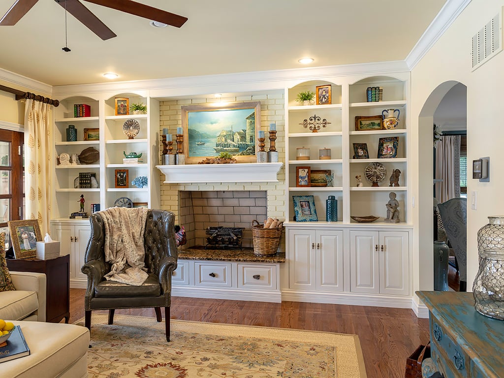 Bright Bethesda living room with built-in white shelves, fireplace, cozy armchair, decorative objects, and landscape painting
