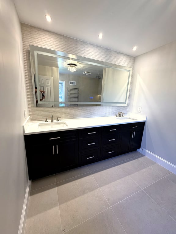A remodeled Potomac bathroom with a dark paneled linen tower, backlit mirror, and a decorative wall sconce