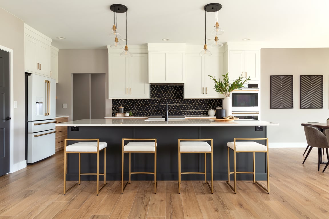 Open-concept kitchen with white inset cabinets, geometric tile backsplash, large island, and brass-legged barstools