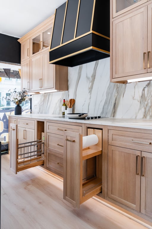 A light-wood kitchen vignette with a black range hood, marble backsplash, and gold hardware in our Bethesda showroom