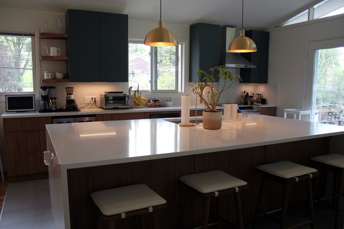 Modern kitchen with dark green upper cabinets, wood lower cabinets, a white waterfall island, and gold pendant lights